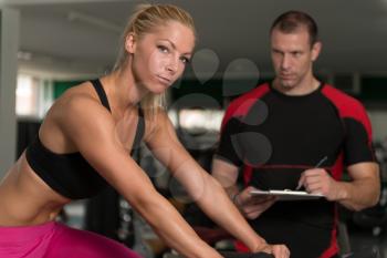 Personal Trainer Showing Young Woman How To Train On Bicycle In The Gym