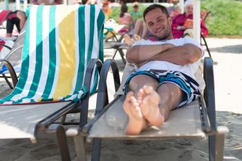 Portrait of Handsome Happy Smiling Man Lying on Chair on Beach by Sea