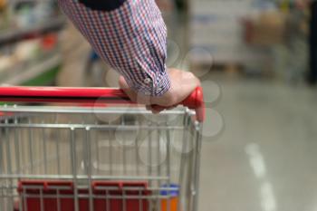 Man Hand Close Up With Shopping Cart in a Supermarket Walking Trough the Aisle