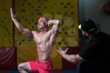 Portrait Of A Man Posing Bodybuilding Poses In Fitness Center and Personal Trainer Corrects Him