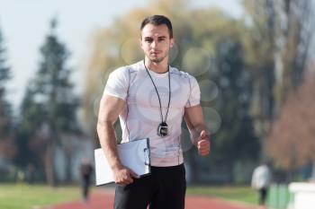 Handsome Personal Trainer With Stopwatch Showing Thumbs Up Sign in City Park Area - Training and Exercising for Endurance - Healthy Lifestyle Concept Outdoor