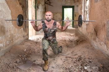 Athlete In Army Pants Working Out Legs Inside Shelter With Barbell