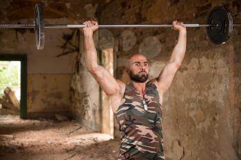 Muscular Man Doing Heavy Weight Exercise For Shoulders With Barbell In Refuge