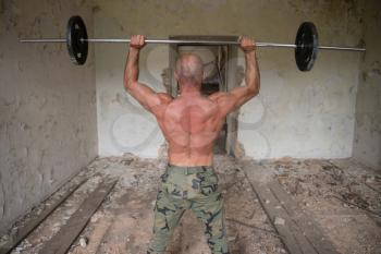Muscular Man Doing Heavy Weight Exercise For Shoulders With Barbell In Refuge