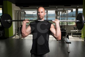 Muscular Man Doing Heavy Weight Exercise For Shoulders With Barbell In Gym