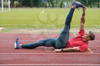 Sporty Man Stretching and Warming Up Legs for Running Fitness Workout on Track Exercising Outside