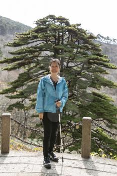 Asian women hiking in Yellow Mountains with large tree and mountains in background
