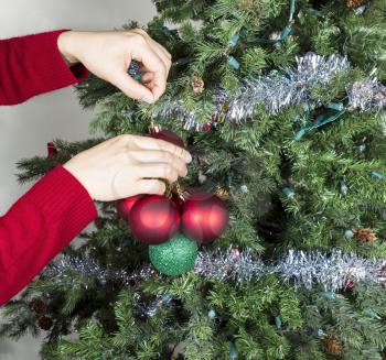 Female hands gathering red and green ornaments to be put into storage with Christmas tree in background