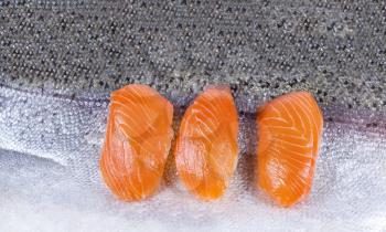 Three pieces of fresh salmon sushi on top of salmon skin