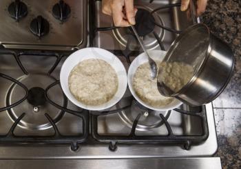 Pouring oatmeal and wheat germ into white bowls on top of stove