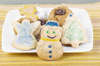 Snowman cookie stands in front of assorted holiday cookies on yellow table cloth