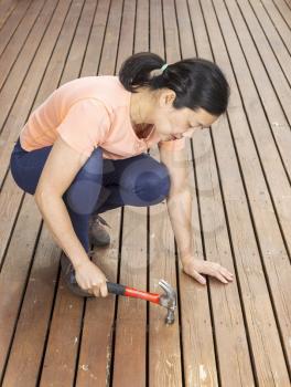 Vertical photo of mature woman adjusting boards with hammer on a natural faded cedar wood deck