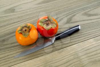 Horizontal photo of dry fresh persimmons with single knife lying on aged white ash wood boards