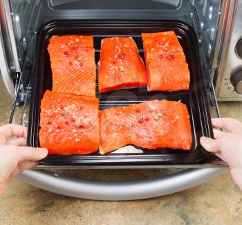 Photo of female hands placing fresh pieces of Wild Red Salmon into oven rack with stone counter top underneath