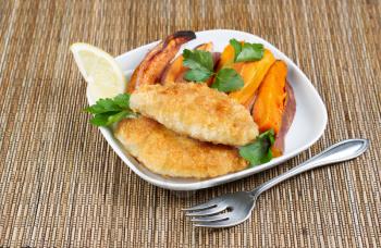 Horizontal photo of fried golden breaded coated fish and yams on white plate