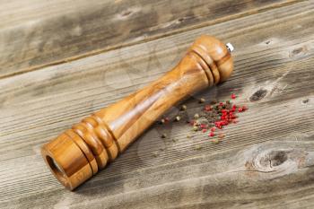Angled photo of a wooden pepper mill with whole dried peppercorns on rustic wood