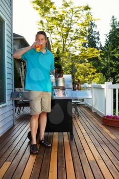 Vertical photo of mature man drinking beer while preparing to barbecue on outdoor cedar wood patio 