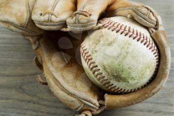 Closeup horizontal photo old dirty baseball inside of heavily used glove on rustic wood 