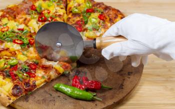 Closeup view of hand wearing white glove cutting gourmet pizza into slices on stone board 