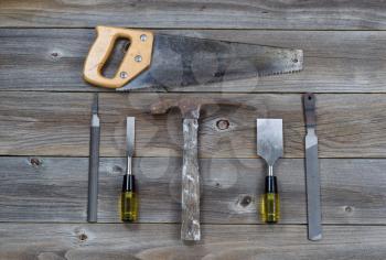 Top view of basic used tools on rustic wooden boards consisting of hammer, metal files, hand saw, and chisels. 