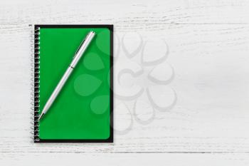 Green spiral notepad with pen on desktop. 