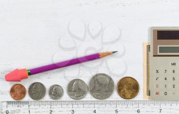 Clear plastic ruler with coins and money reflecting the concept of measuring investments along with a calculator and pencil with eraser on desktop.