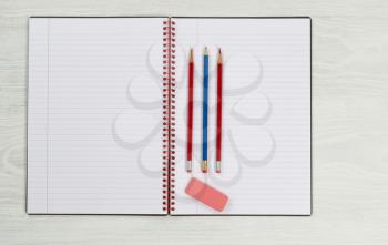 Blank new notepad, in open position, with sharpen pencils and eraser on rustic white desktop. 
