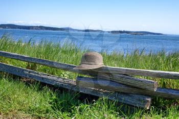 Image of a leisure hat resting on rustic wooden split rail fence with ocean and sky in background. 