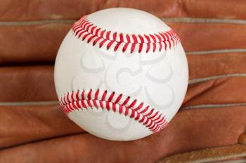 Close of baseball, selective focus on center, with leather mitt in background. Format in filled frame layout. 