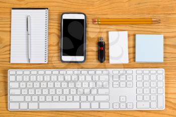 High angled view of a highly organized desktop consisting of computer keyboard, pencils, pen, cell phone, notepad, business cards and thumb drive. Horizontal layout. 