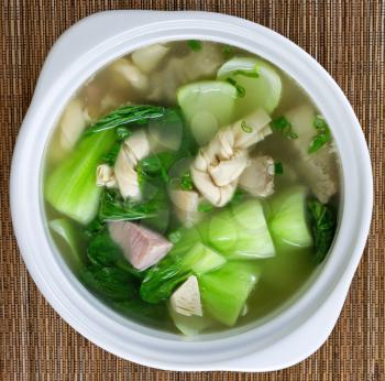 High angled view of Asian soup consisting of pork, dumpling and bok choy vegetable on bamboo mat. 