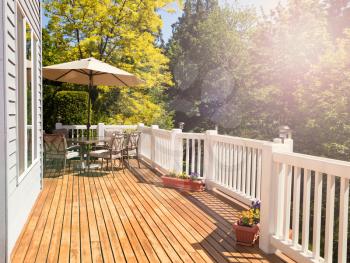Afternoon bright daylight on outdoor home cedar deck with furniture and open umbrella. Light effect applied to image. Horizontal layout. 