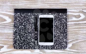 Notepad, pen and cell phone on top of faded white wooden desktop. Overhead view of display. 