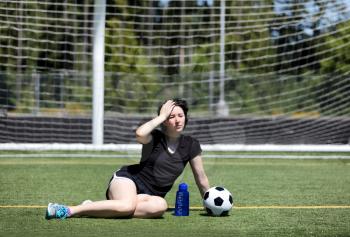 Teen age girl holding her head while resting on the soccer field during a hot day 