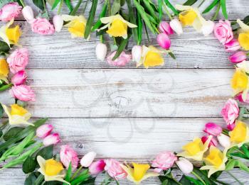 Assortment of spring flowers forming heart shape on white rustic wooden boards 