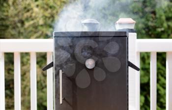 Close up of a cooking smoker with woods in background