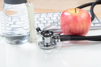 Medical health care concept consisting of traditional stethoscope and apple with bottled water in background 