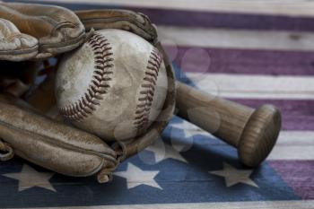 Closeup view of an old baseball, glove and traditional wood bat on rustic wooden United States Flag