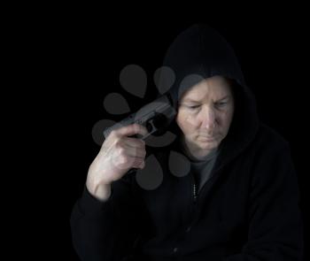 Depressed mature man ready to commit suicide with gun pointed to side of head while surrounded in darkness 