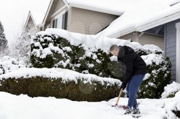 Mature man shoveling snow off sidewalk in front of home 