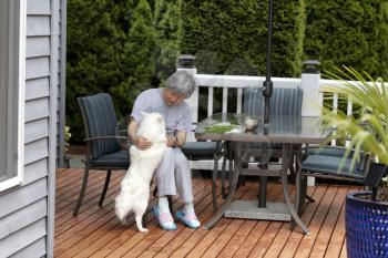 Senior woman enjoying the company of her pet dog would working outside on the home deck  