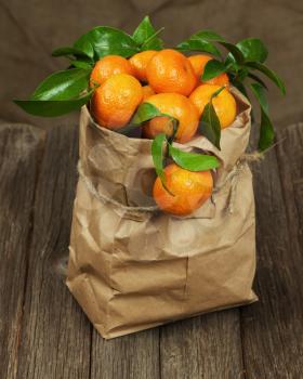 Fresh tangerines with leaves in recycle paper bag on wooden table.