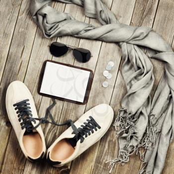 Set of travel items including scarf, sunglasses, sneakers, note book and money. Different travel objects and passenger luggage on grey wooden background. Top aerial view. 