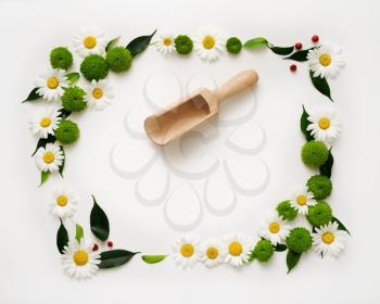 Wooden scoop and space for your text or product with decoration of chrysanthemum flowers and ficus leaves on white background. Overhead view. Flat lay.