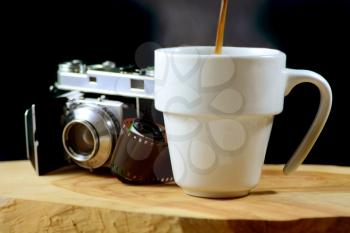 Macro shot of a steaming cup of coffee with an analog camera and roll of film in the background