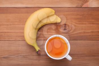 A cup of hot tea and bananas on a wooden background.