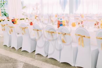 Decorative White Mantles And Colored Ribbons On Chairs At Festive Table. Chairs And Table Covered With Cloth.