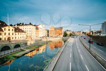 Stockholm, Sweden. The View Of Embankment Along Water Channel And Centralbron Highway  In Gamla Stan In Summer Sunny Evening.