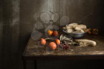 still life with fruit and corn in an aluminum bowl on a wooden old table