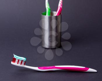 A pink toothbrush with toothpaste on a grey background